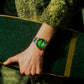 Hand wearing a watch with a green face on a green background. Seiko x HUF